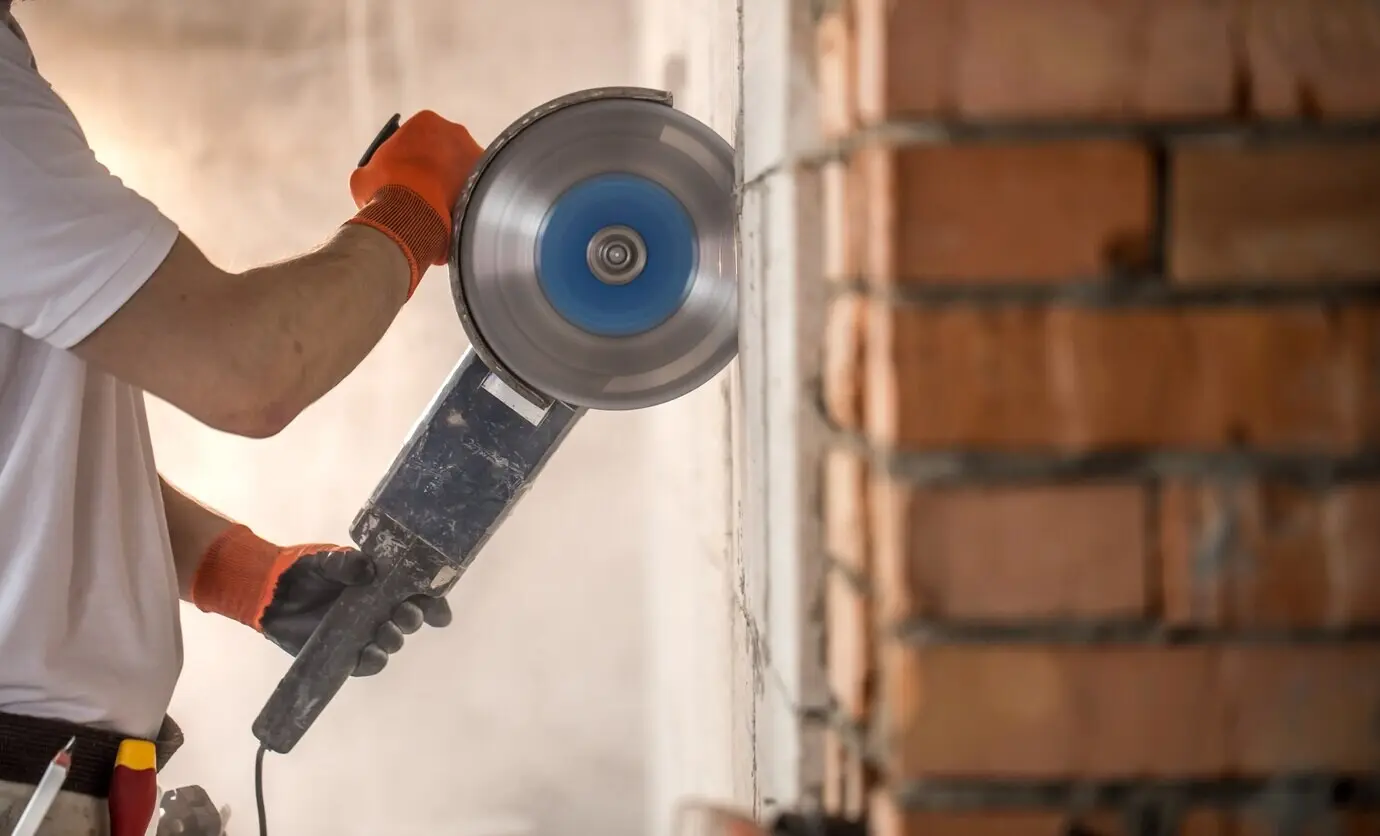 An industrial builder operates a professional angle grinder to cut bricks and construct interior walls. Electrician.